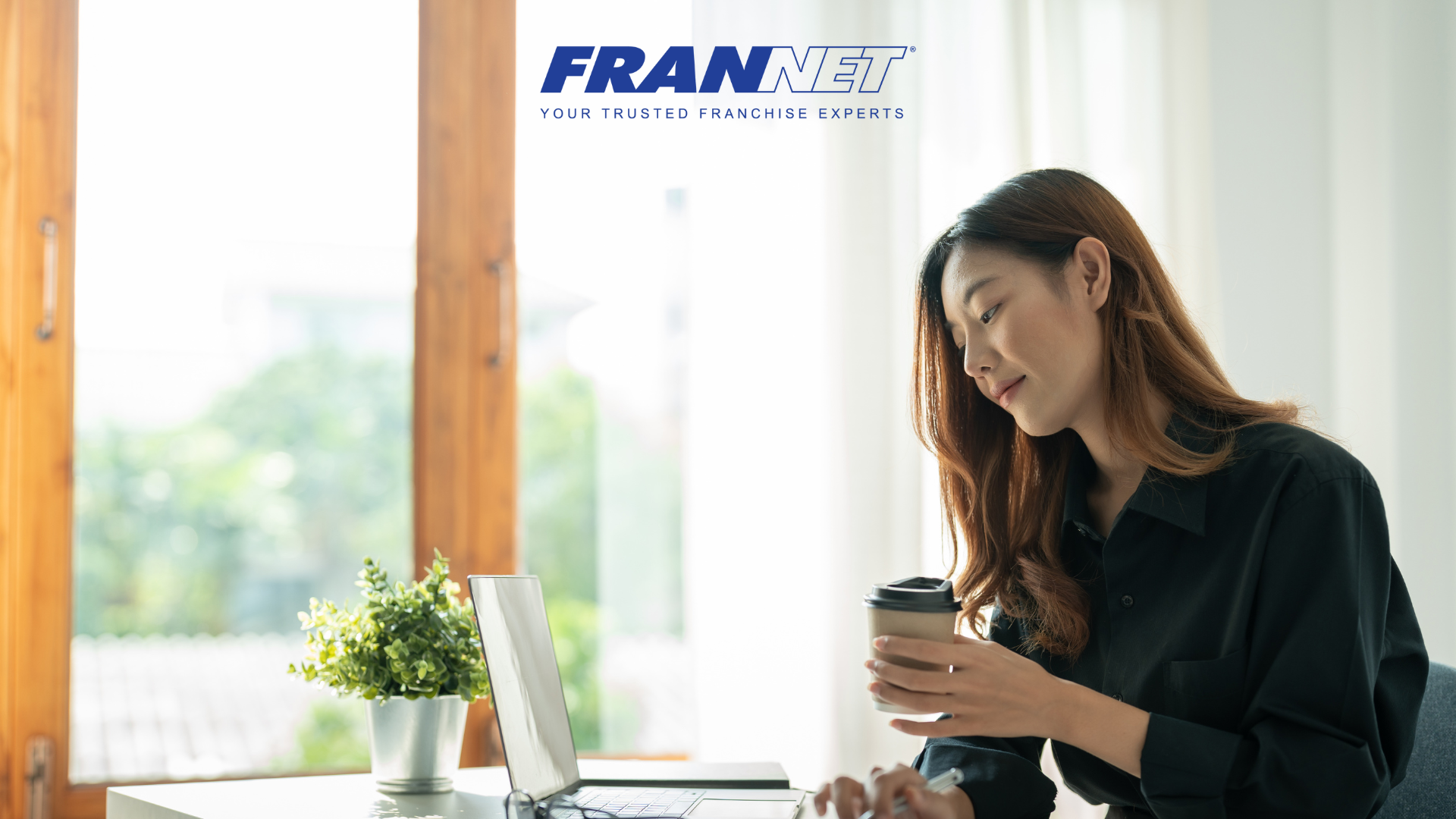 Girl holding coffee working at laptop at home