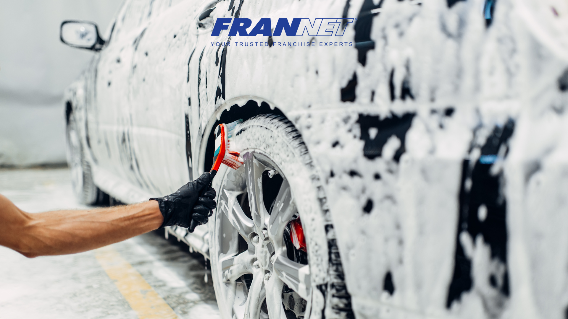 Someone scrubbing tires of a soapy car getting washed and detailed