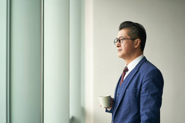 Portrait Of A Asian Business Leader Senior Manager Standing By Window Thinking