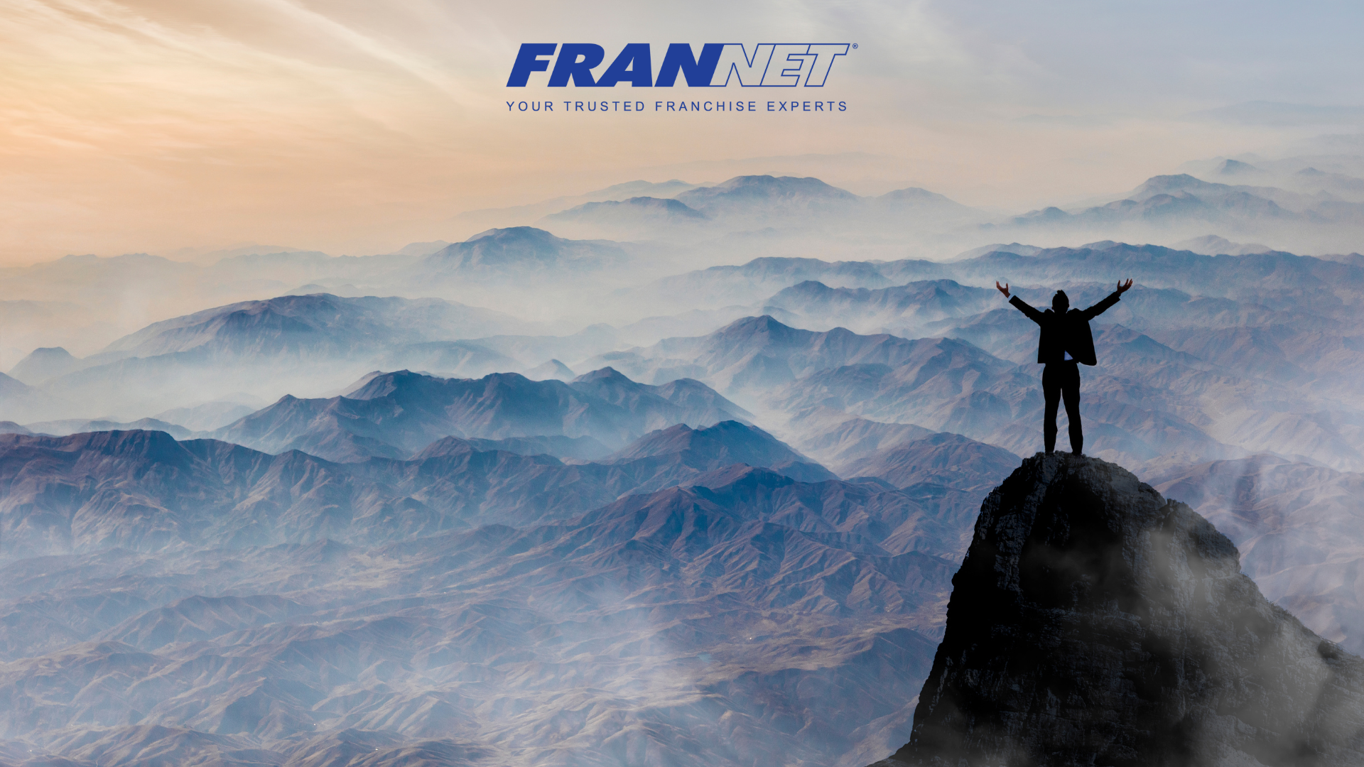 Man standing on high edge of mountain with arms raised representing franchise success rates
