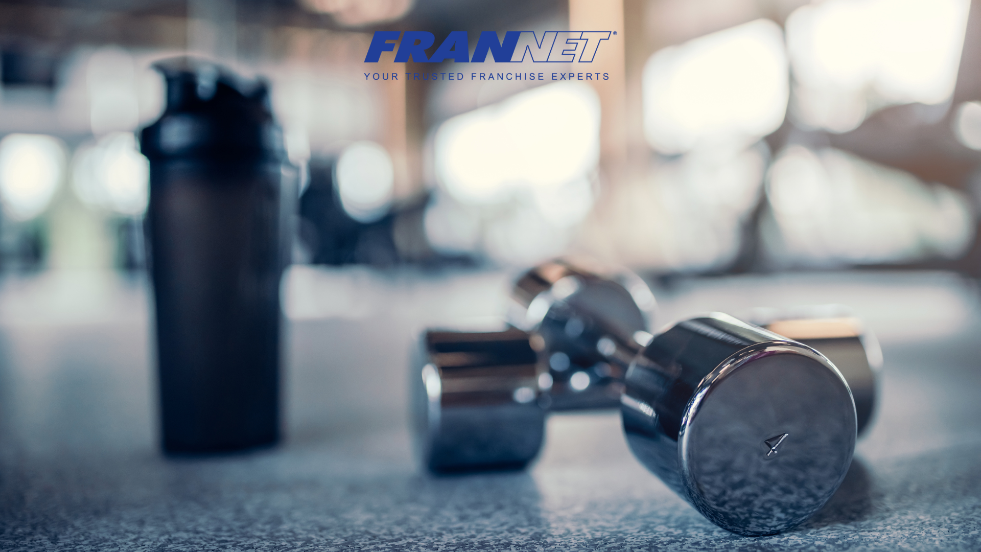 Dumb bells next to water bottle with gym in background