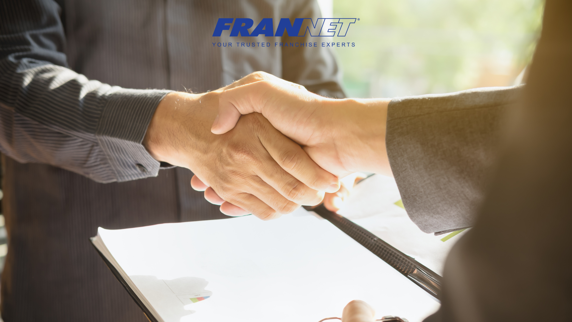 Two people shaking hands while holding document