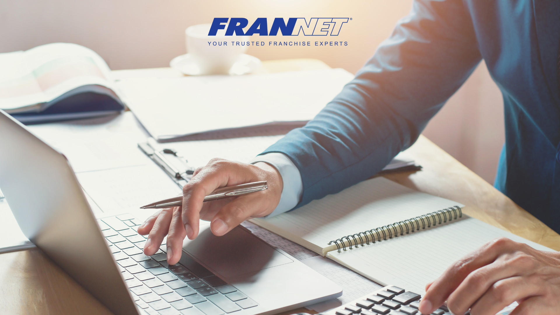 Person sitting at desk with pen in hand working at the laptop