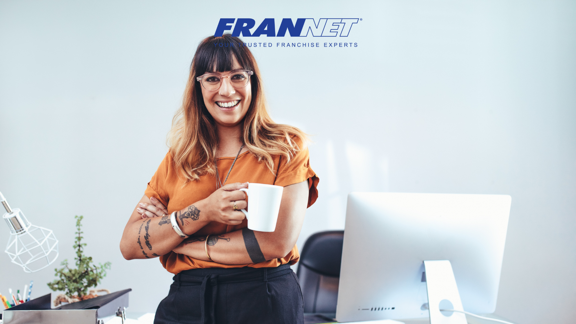 Female entrepreneur smiling holding a cup of coffee standing in front of desk and computer - entrepreneurs who want to open a franchise