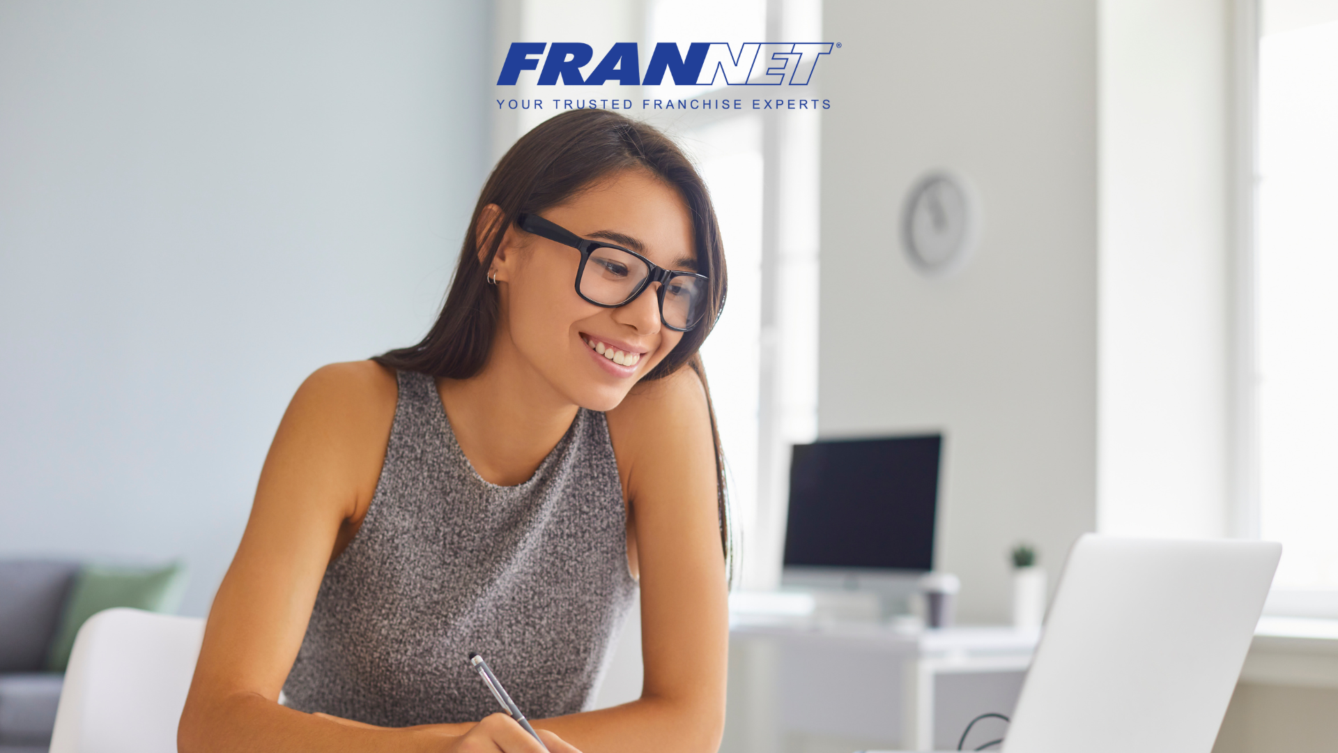 Woman smiling looking at computer while holding a pen