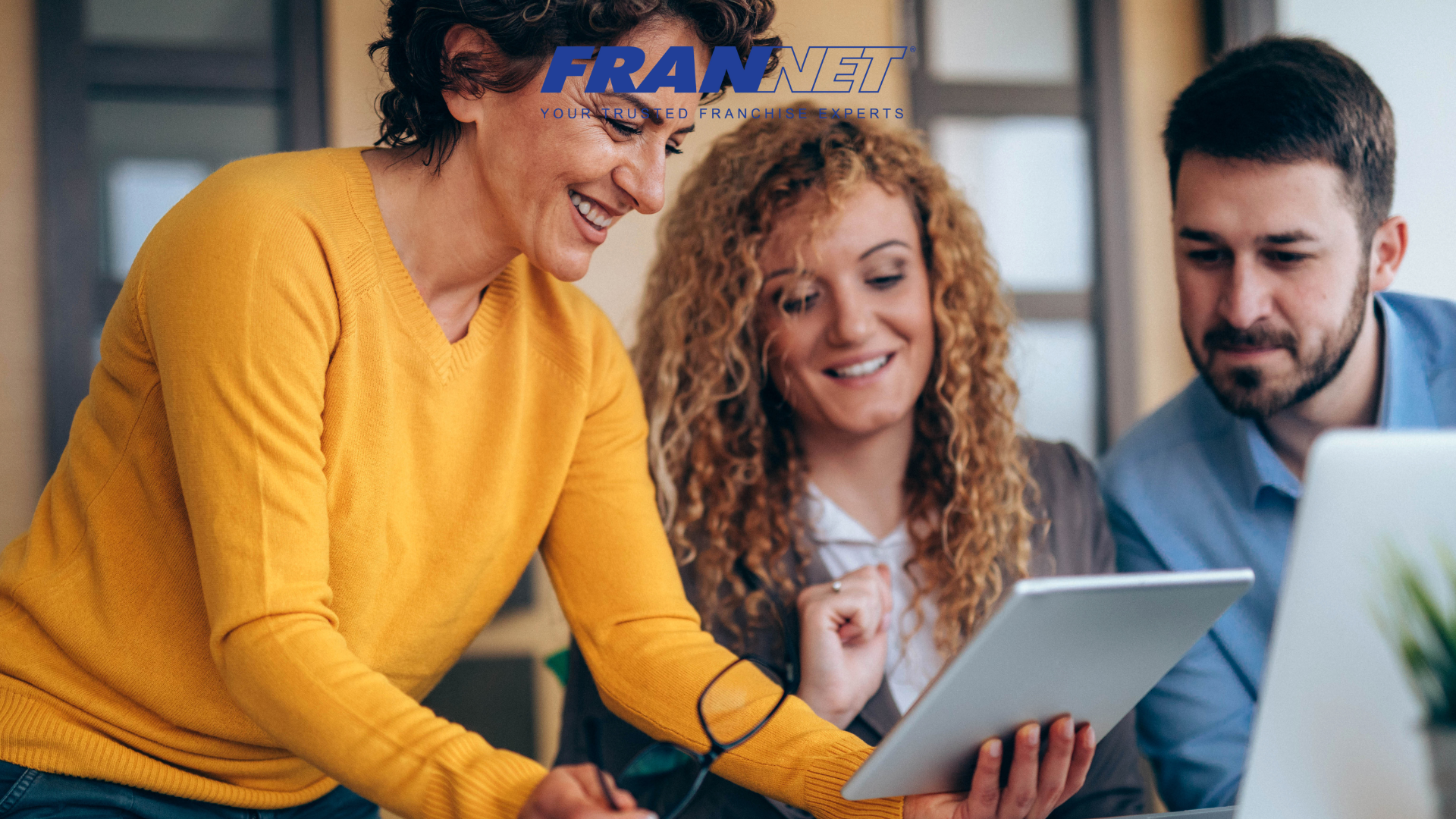 Three people looking at tablet together while in front of a computer