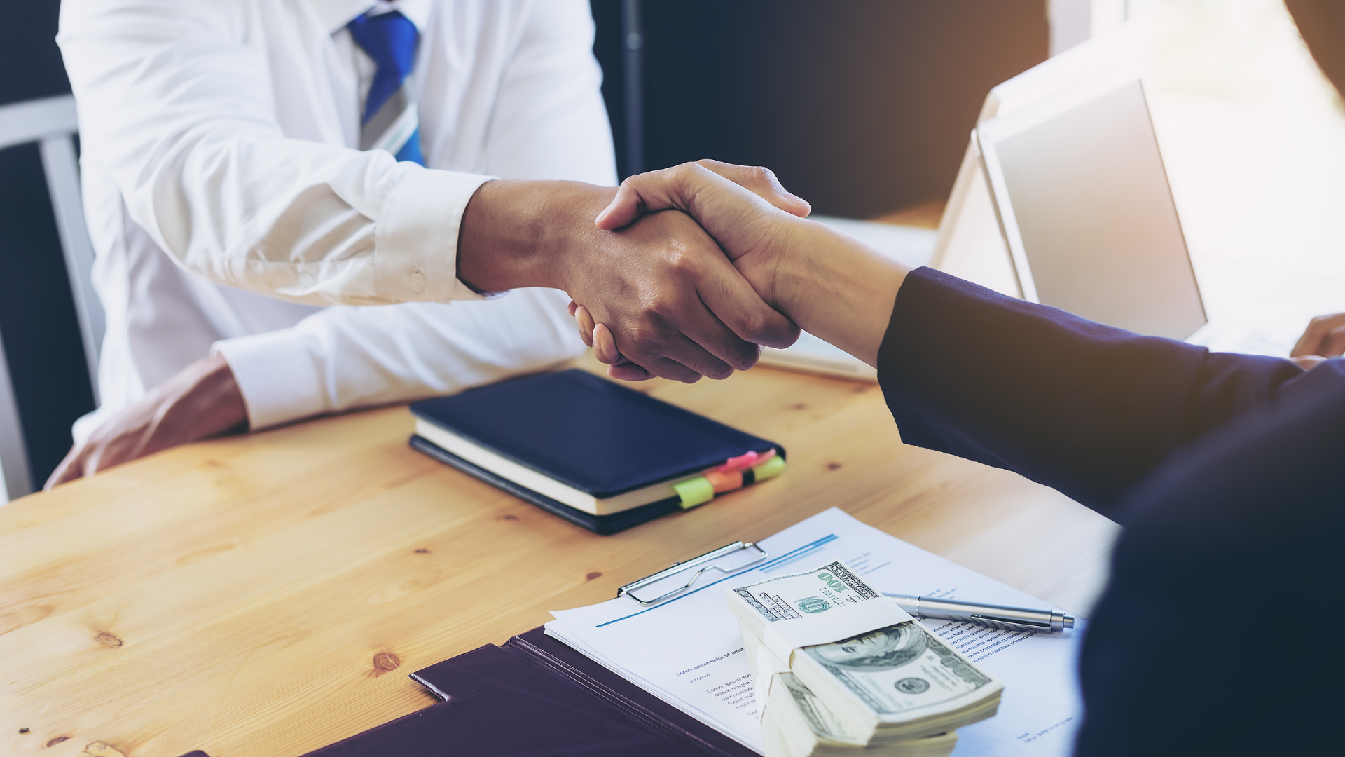 Two people shaking hands with money on the desk - representing how to get a business loan for a franchise